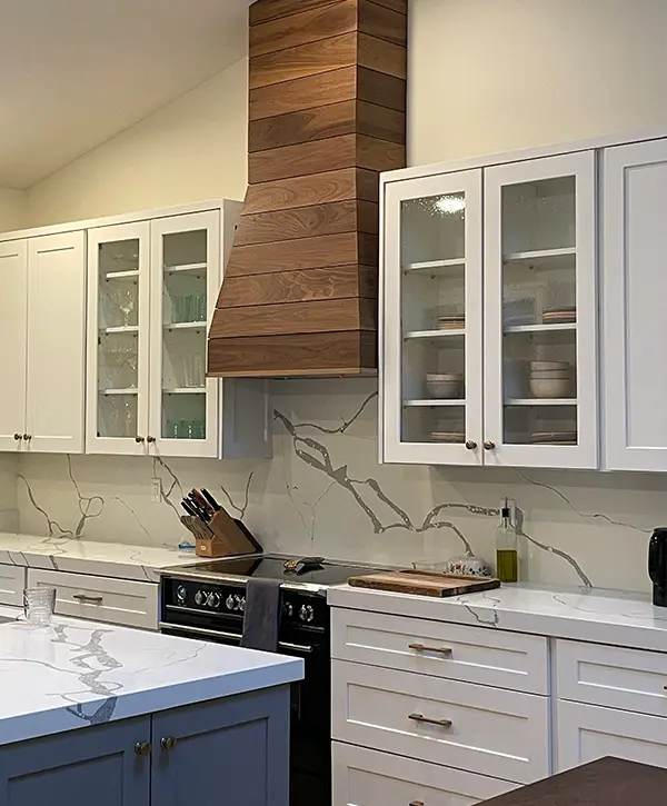 Luxury kitchen design with wood vent hood, glass-front cabinets, and quartz countertops